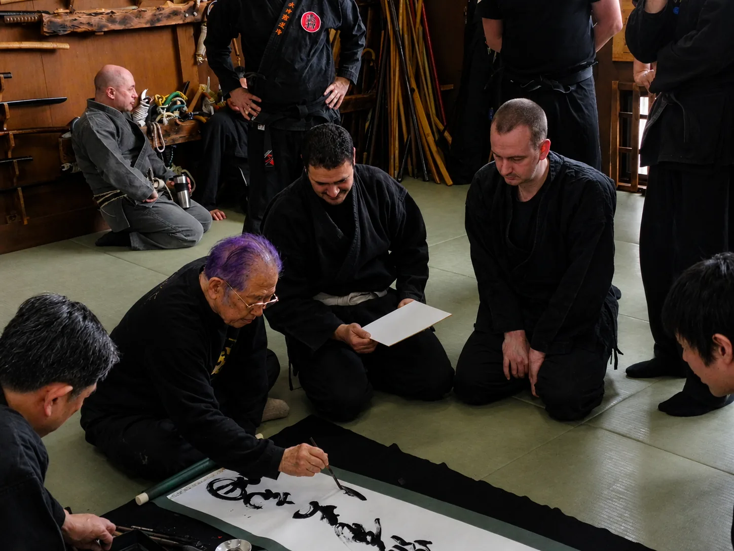 Hatsumi Sensei réalisant une calligraphie japonaise au dojo, entouré de ses élèves